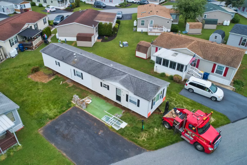 Aerial view of manufactured home being dropped off or moved by red truck in mobile home park